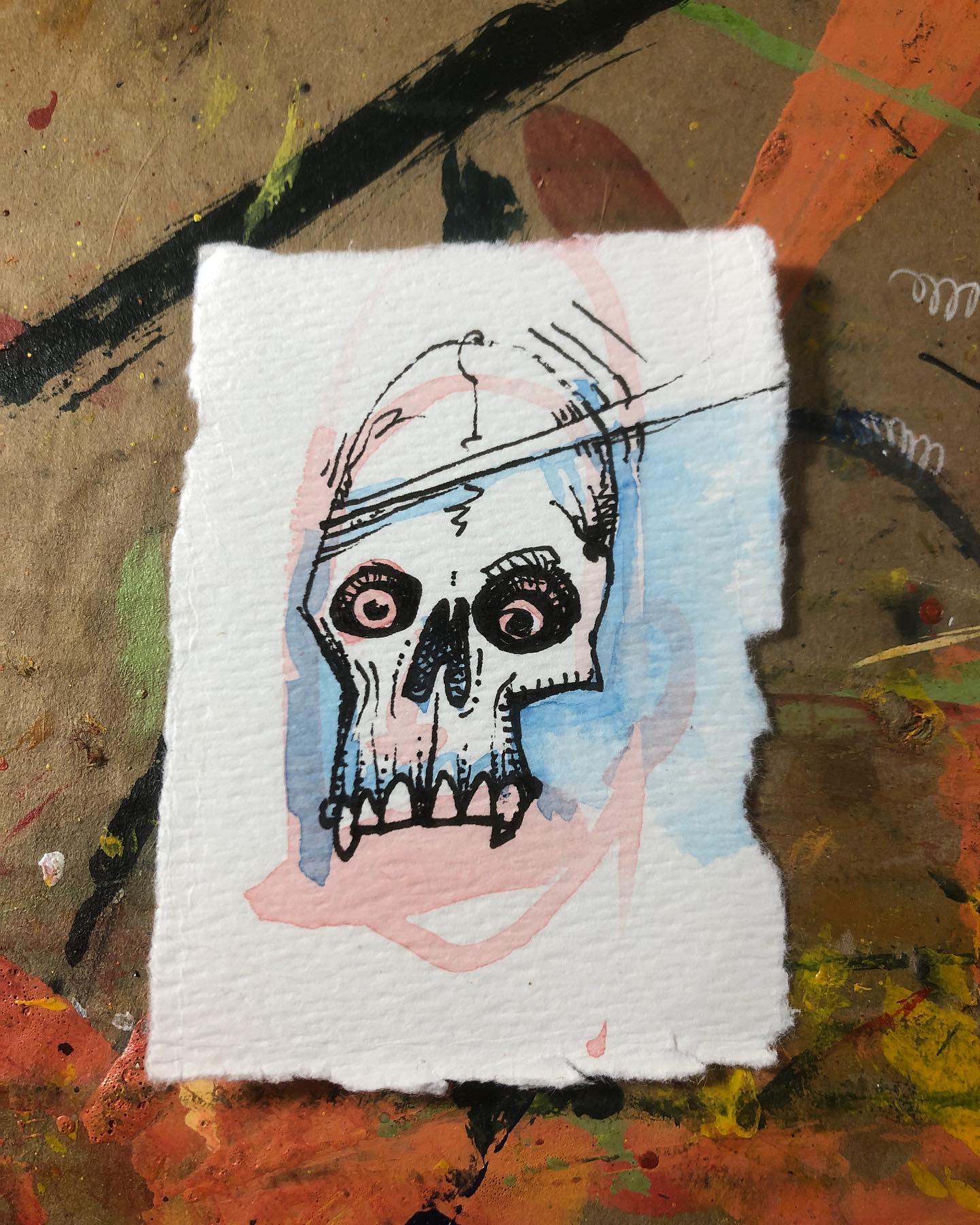 Ink drawing of a skull with blue/pink watercolor accents